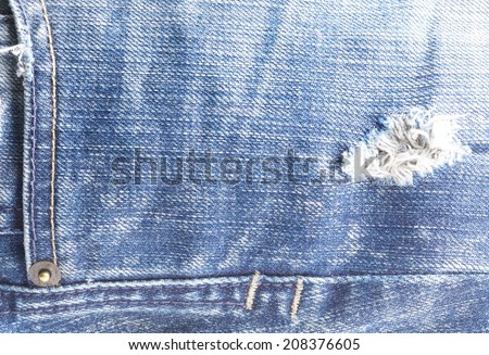 Blue denim jeans in bright color tear up surface near the front pocket in the scene show the brass rivet present the old damaging fabric damaged detail of texture background.