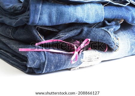 Blue denim jeans many pairs in dark color tone fold and stack up together. In the scene present the black color pantie with pink ribbon between the layer of folding jeans.