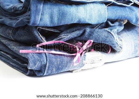 Blue denim jeans many pairs in bright color tone fold and stack up together. In the scene present the black color pantie with pink ribbon between the layer of folding jeans.