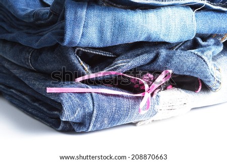 Blue denim jeans many pairs in bright color tone fold and stack up together. In the scene present the black color pantie with pink ribbon between the layer of folding jeans.
