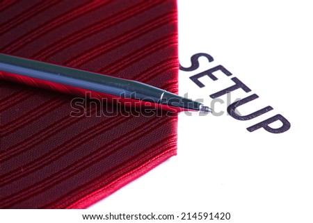 Red color of necktie close up photo in the scene with the white paper color printed the word set up put beside show the pattern and texture fabric of  necktie represent the formalwear business look.