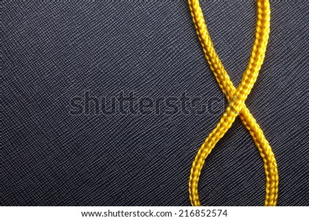 Gold color rope cable with simple knot close up photo put on the black color artificial leather surface background.
