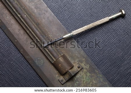 Old and vintage brass slide rule and screwdriver put on the black color artificial leather surface background.