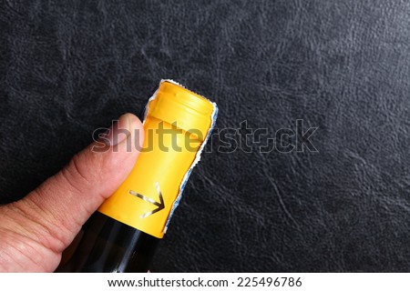 Wine bottle in closing cap condition focus at the neck of the bottle and man hand to see the yellow color with golden arrow neck bottle label and tax stamp.