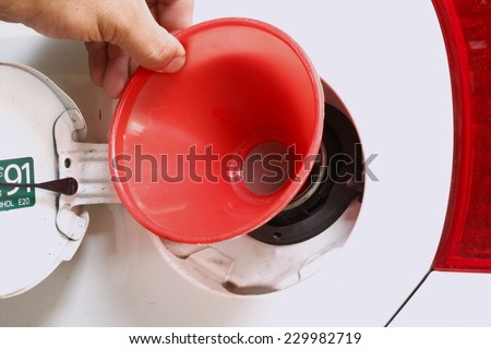 Man hand in action of holding the red color plastic fuel funnel in the scene focus at the car fuel tank lid.