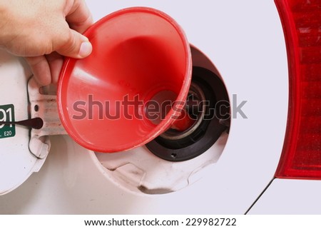 Man hand in action of holding the red color plastic fuel funnel in the scene focus at the car fuel tank lid.