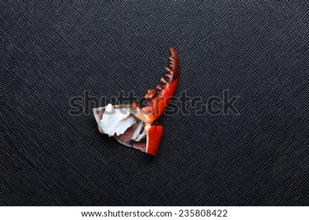 The claws of the crab with orange color put on the black color leather surface background  represent the crab body part and food left over meaning.