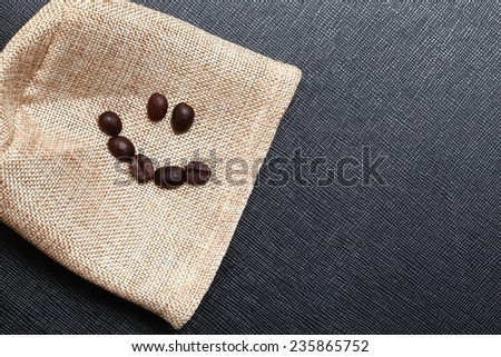 Coffee bean arrange to the shape of smiling face put on the coffee bean sack in the scene appear the back color leather background.