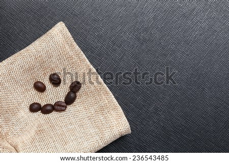 Coffee bean arrange to the shape of smiling face put on the coffee bean sack in the scene appear the back color leather background.