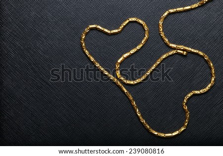 Gold necklace arrange to the heart shape pattern put on black color leather background represent the abstract meaning