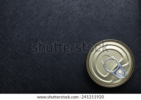 Closed canned food put on black color leather surface background represent the food containing material.