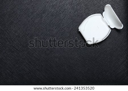 Dental floss in white color plastic containing box put on black color leather surface background represent the dental care equipment.