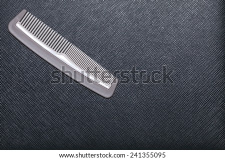 Plastic comb grey color put on black color leather surface background represent the hairdressing equipment material.