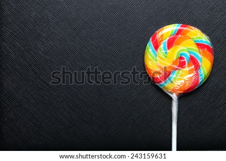 Colorful lollipop new with plastic packaging wrapped and white stick put on the black color leather background represent the sweet candy.