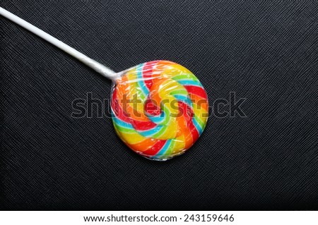 Colorful lollipop new with plastic packaging wrapped and white stick put on the black color leather background represent the sweet candy.