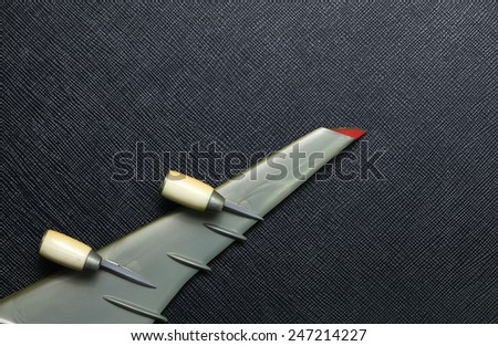 Old plastic airplane model focus at wing and turbine engine part put on the black color leather surface background represent the airplane part.