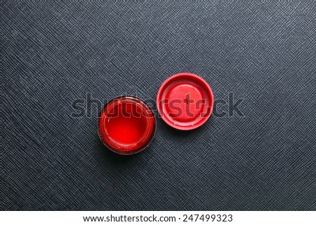 A bottle of red color for plastic model paint with bottle lid put on the black color leather surface background represent the model making material.