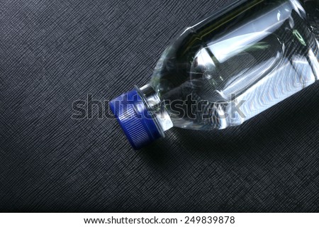 Drinking water bottle with blue color cap made from transparent food grade plastic put on the black color leather background represent the water containing material related.