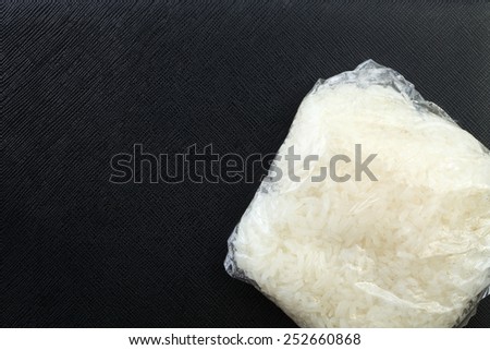 Sticky rice in the food grade plastic containing bag put on the black color leather surface background represent the food and food packaging related.