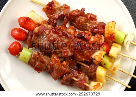 Barbecue beef and chicken with one stick missing tomato on top of the stick ready to serve on the beige color plate put on the black color leather surface background represent the cooked food related.