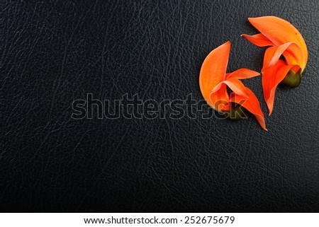 Orange color flower put on the black color leather surface background represent the flora shape pattern idea and concept related.