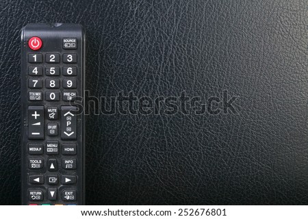 Used and dirty tv remote control put on the black color leather surface background represent the tv technology related.