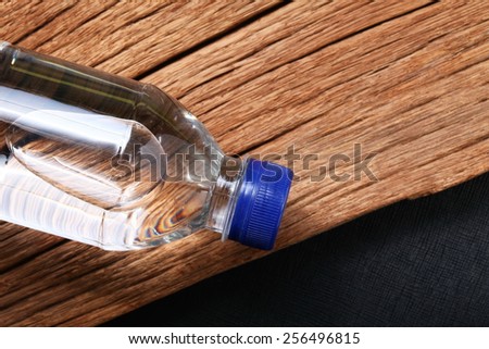 Drinking water bottle with blue color cap made from transparent food grade plastic put on the haed wood background represent the water containing material related.