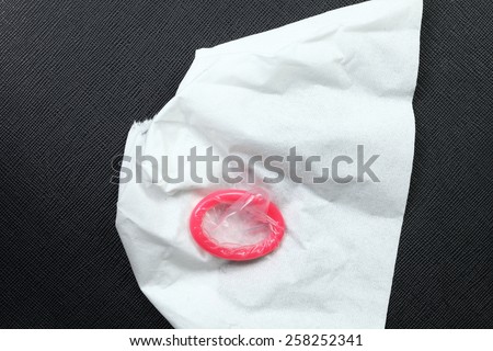 Pink color condom and tissue paper put o put on the black color leather background represent the sex education concept idea related.