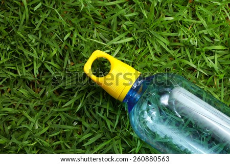 Drinking water bottle with yellow color cap made from transparent food grade plastic put on the grass background represent the water containing material related.