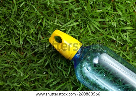 Drinking water bottle with yellow color cap made from transparent food grade plastic put on the grass background represent the water containing material related.