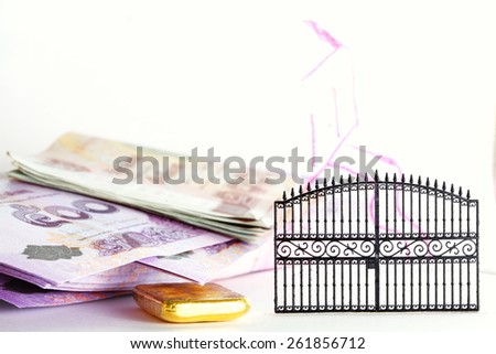 Thailand banknotes and gold bar put beside the plastic gate model in the scene appear the hand drawing house shape on clear acrylic surface represent the mortgage concept idea.