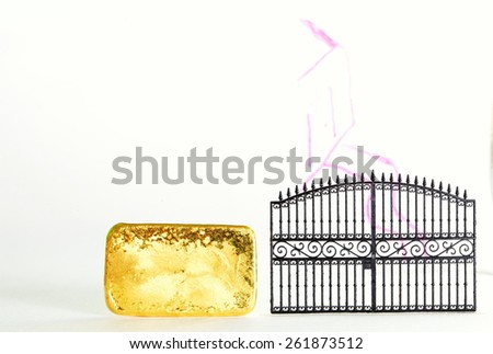 Gold bar beside the plastic gate model in the scene appear the hand drawing house shape on clear acrylic surface represent the mortgage concept idea.