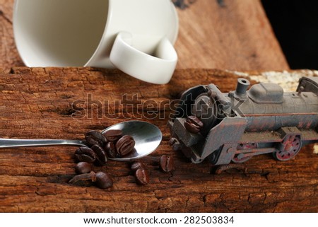 Coffee beans on old hard wood with old and dirty model train toy represent coffee business concept related idea . Super macro shot and intention focus at the train.