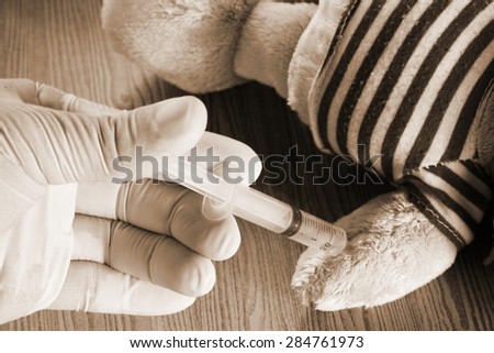 Hand in medical rubber glove with injection action to doll in sepia tone represent the medical care concept related idea.