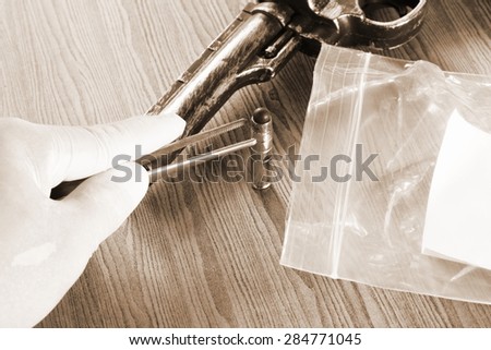 The artificial vintage plastic toy gun beside forceps in action of holding bullet on sepia tone represent crime science investigation instrument concept related idea