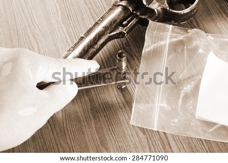 The artificial vintage plastic toy gun beside forceps in action of holding bullet on sepia tone represent crime science investigation instrument concept related idea