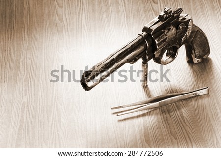 The artificial vintage plastic toy gun beside forceps on sepia tone represent crime science investigation instrument concept related idea