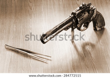 The artificial vintage plastic toy gun beside forceps on sepia tone represent crime science investigation instrument concept related idea