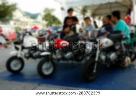 Blurry photo of man sit behind motorcycle on car booth selling area in the open market scene represent the people lifestyle concept related idea.
