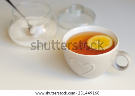 Grey ceramic cup with heart decoration, black tea and lemon on white background