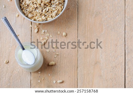 Glass jar with yogurt without sugar and ceramic bowl with oat granola and peanuts