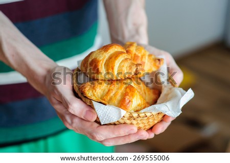 Man holding straw bowl with fresh baked croissants