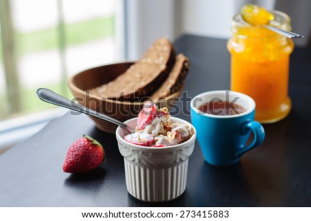 Cup of granola with strawberry and yogurt, coffee, orange jelly
