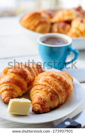 Breakfast with fresh baked croissants, butter and coffee on white wooden background