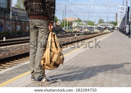 Young man waits train on railway platform