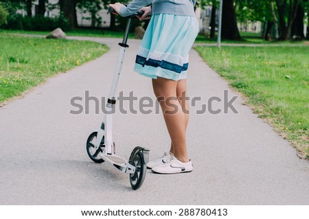 Legs of young woman in dress on kick scooter