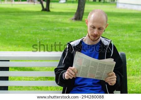 Young man reads  newspaper on a bench in park