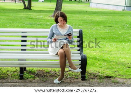 Young woman reads newspaper on a bench in park