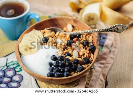 Homemade oatmeal granola with peanuts, blueberry and banana in wooden bowl, sunny morning