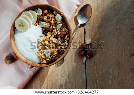 Homemade oatmeal granola with peanuts, blueberry and banana in wooden bowl, sunny morning